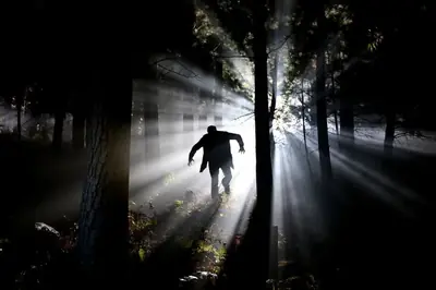 Siluett av en person som springer genom mörk skog, som jagad