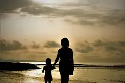 Siluett av en mamma och ett barn som går längs stranden