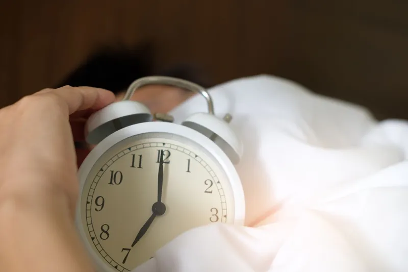En hand på väckarklockan i en bädd på morgonen
